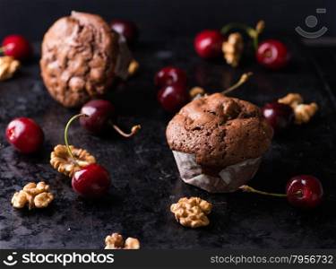 Chocolate muffins on dark background, walnuts, cherries and chocolate chunks as decoration, selective focus