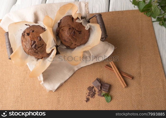 Chocolate muffins with chocolate slices in basket, cinnamom sticks and mint on placemat