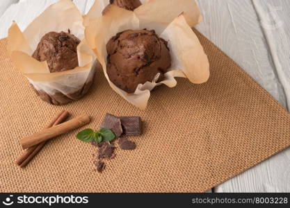 Chocolate muffins with chocolate slices in basket, cinnamom sticks and mint on placemat