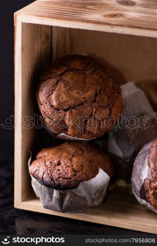 Chocolate muffins with nuts in wooden box, on dark background, selective focus