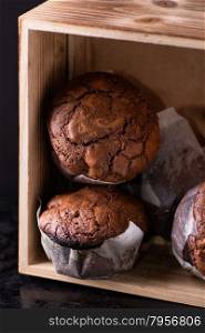Chocolate muffins with nuts in wooden box, on dark background, selective focus