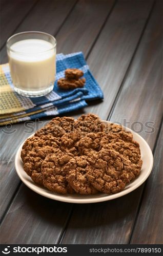 Chocolate oatmeal cookies on plate with a glass of milk in the back, photographed with natural light (Selective Focus, Focus on the first cookies)