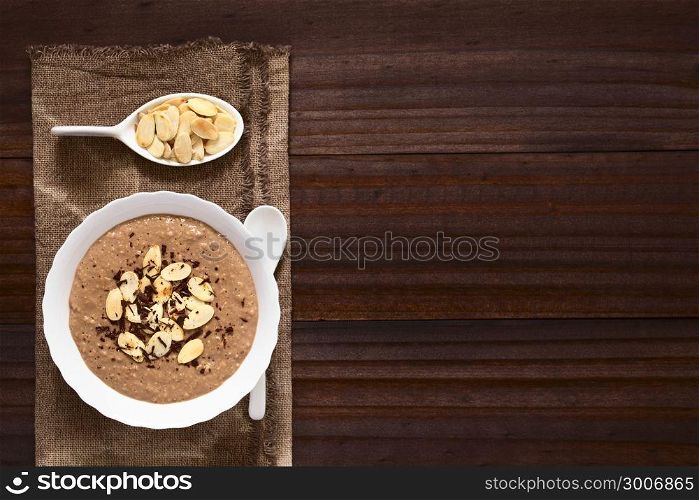 Chocolate oatmeal or oat porridge with toasted almond slices and grated chocolate on top served in small bowl, photographed overhead with natural light (Selective Focus, Focus on the porridge). Chocolate Oatmeal or Oat Porridge