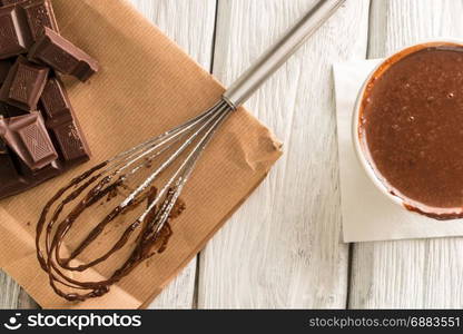 Chocolate on egg beater and chocolate parts on wooden table top