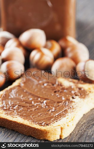 Chocolate over rusk, with hazelnuts and jar on the background, focus on first part of rusk, vertical image