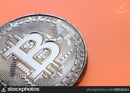 Chocolate product in the form of physical bitcoin lies on an orange plastic background. Model of the crypto currency in the edible form