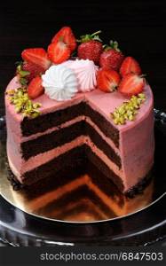 Chocolate strawberry cake decorated with berries, meringue and pistachios in a cut