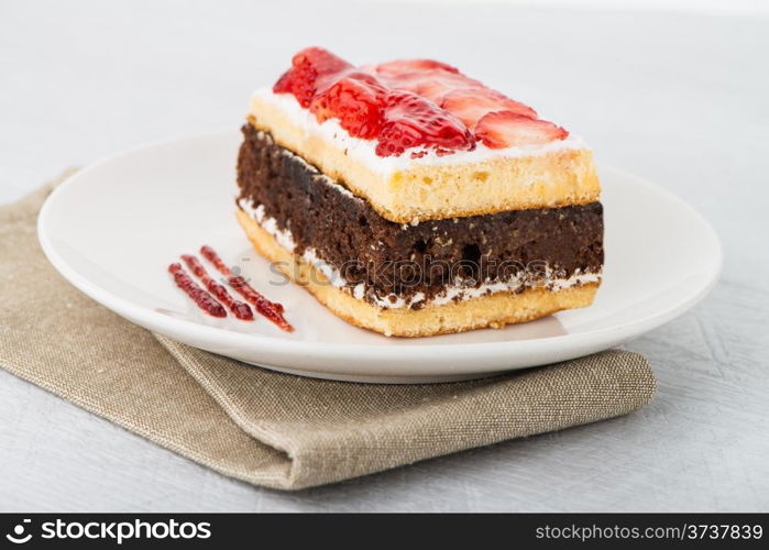 Chocolate strawberry cake on white plate and wooden table.