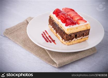 Chocolate strawberry cake on white plate and wooden table.