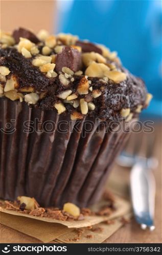Chocolate-walnut muffin with coffee cup in the back (Selective Focus, Focus on the front edge of the muffin)