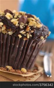Chocolate-walnut muffin with coffee cup in the back (Selective Focus, Focus on the front edge of the muffin)