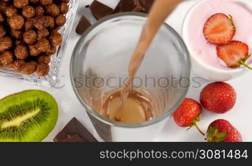Chocolate with milk flowing in glass for breakfast in slow motion. Healthy eating for breakfast with fruits, cereals and yogurt.