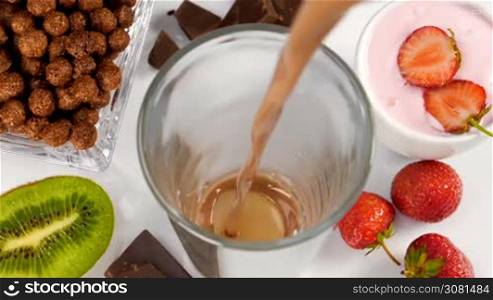 Chocolate with milk flowing in glass for breakfast in slow motion. Healthy eating for breakfast with fruits, cereals and yogurt.