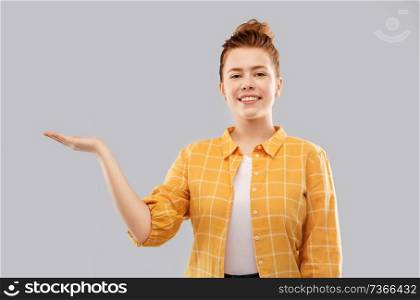 choice and people concept - red haired teenage girl in checkered shirt holding something imaginary on empty hands over grey background. red haired teenage girl holding empty hands