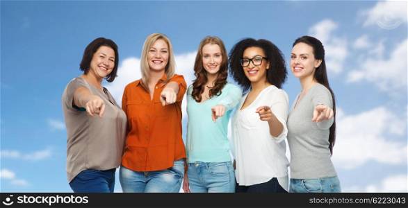 choice, friendship, fashion, diverse people concept - group of happy plus size women in casual clothes pointing finger on you over blue sky and clouds background