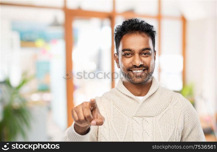 choice, gesture and people concept - smiling indian man pointing finger to camera over office background. smiling indian man pointing finger to camera