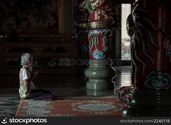 Chonburi, Thailand - 05 Feb 2022 : Senior woman sitting praying pay respect to Buddha statue in the Wihan Thep Sathit Phra Ki Ti Chaloem ( San Chao Na Cha ). Focus and blur.