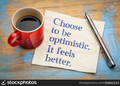 Choose to be optimistic.. It feels better. Handwriting on a napkin with a cup of espresso coffee