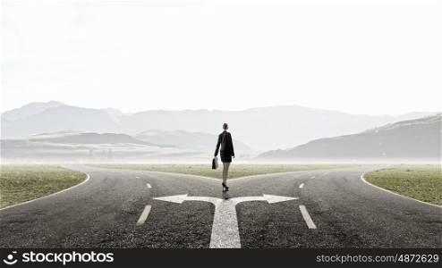 Choose your way. Back view of businesswoman standing on crossroads and making choice
