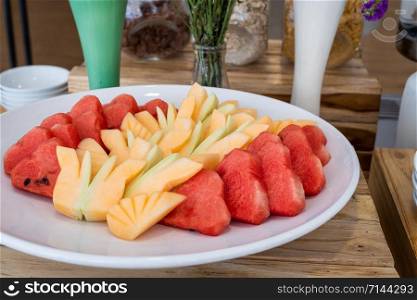 Chop the pieces of watermelon and pineapple in white dish the dining and flower vase on table decorationat buffet self service at hotel.