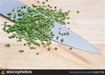 Chopped chives on wooden chopping board with sharp knife