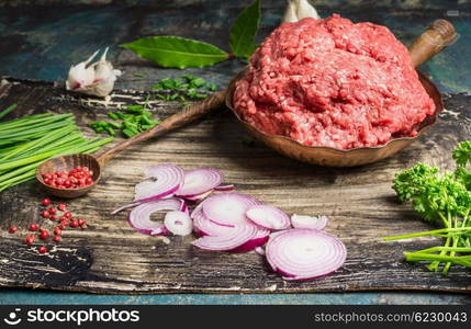 Chopped meat in pan with wooden spoon and ingredients for tasty cooking on rustic kitchen table