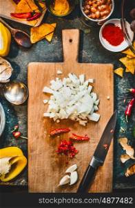 Chopped onion, chili and garlic on wooden cutting board with knife . Spicy mexican cuisine on rustic kitchen table background with canned beans and ingredients, top view.