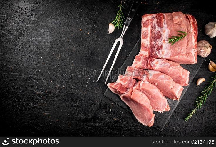 Chopped raw pork on a stone board with rosemary and garlic. On a black background. High quality photo. Chopped raw pork on a stone board with rosemary and garlic.