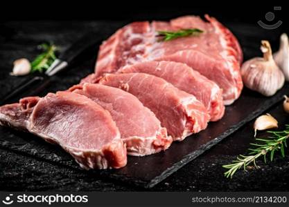 Chopped raw pork on a stone board with rosemary and garlic. On a black background. High quality photo. Chopped raw pork on a stone board with rosemary and garlic.