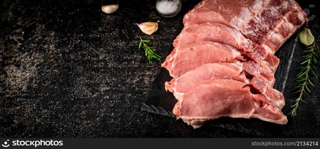 Chopped raw pork on a stone board with rosemary and garlic. On a black background. High quality photo. Chopped raw pork on a stone board with rosemary and garlic.