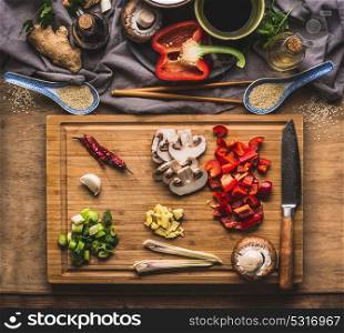 Chopped vegetables for stir fry cooking on wooden cutting board on kitchen table background with ingredients, top view. Asian food and eating , Chinese or Thai cuisine concept