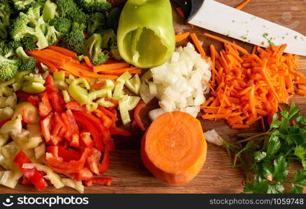 chopped vegetables peppers, broccoli, onions, carrots on a wooden board, top view