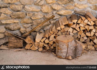 Chopped wood and axe stacked against the stone wall of a rustic farmhouse. Stack of firewood against stone wall of farmhouse