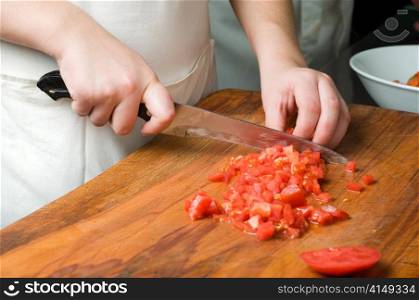 chopping the tomato using big knife on the wooden cutting board. chopping the tomato