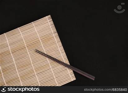 Chopsticks on bamboo matt on black background. Oriental serving.