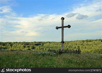 Christian wood cross on grass overgrown hill (and forest colony far away)