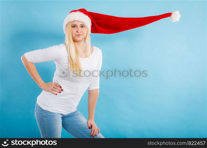 Christmas accessories, fun and joy concept. Woman wearing windblown long Santa hat, fooling around. Studio shot on blue background. Woman wearing windblown long Santa hat