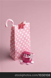 Christmas Advent calendar in pink concept. Gift paper bag with a candy cane and present box with candies on a pink background. Xmas Advent surprises