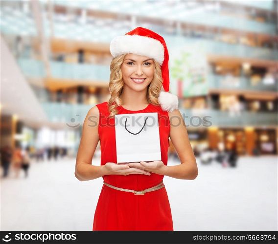 christmas, advertisement, holydays and sale concept - smiling woman in santa helper hat with white blank shopping bag over shopping center background