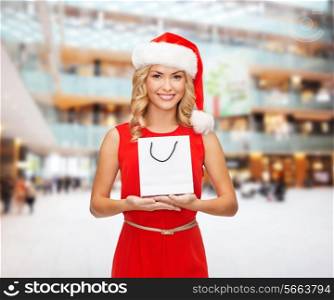 christmas, advertisement, holydays and sale concept - smiling woman in santa helper hat with white blank shopping bag over shopping center background