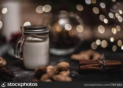 Christmas and new year celebration table decoration background with round bokeh garland, cinnamon, cookies, cones, nuts and candle in cup. Christmas and new year decoration background with round bokeh garland, cinnamon, cookies, cones, nuts and candle in cup