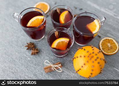 christmas and seasonal drinks concept - glasses of hot mulled wine with orange and cinnamon on grey background. glasses of mulled wine with orange and cinnamon