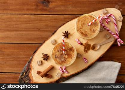 christmas and seasonal drinks concept - glasses with eggnog, ingredients and aromatic spices on cut wood board. glasses of eggnog, ingredients and spices on wood