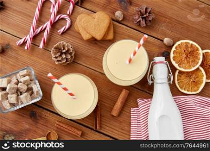 christmas and seasonal drinks concept - glasses with eggnog, ingredients and aromatic spices on wooden background. glasses of eggnog, ingredients and spices on wood