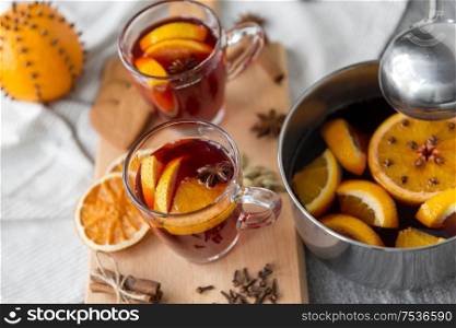 christmas and seasonal drinks concept - glasses with hot mulled wine, orange slices, aromatic spices and pot on grey background. pot with hot mulled wine, orange slices and spices