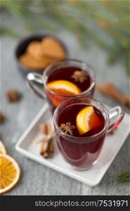 christmas and seasonal drinks concept - hot mulled wine, dry orange slices, gingerbread and aromatic spices on grey background. mulled wine, orange slices, gingerbread and spices