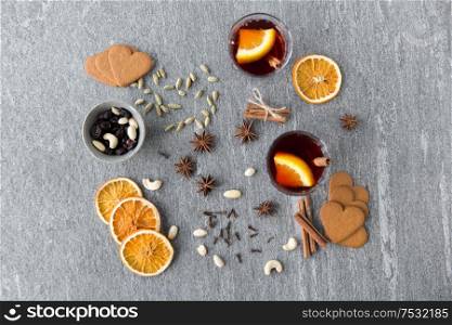 christmas and seasonal drinks concept - hot mulled wine, dry orange slices, raisins with cashew nuts and aromatic spices on grey background. hot mulled wine, orange slices, raisins and spices