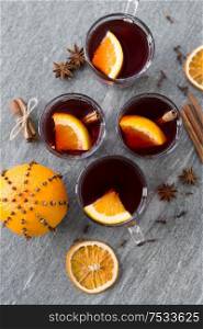 christmas and seasonal drinks concept - hot mulled wine, dry orange slices, raisins with cashew nuts and aromatic spices on grey background. hot mulled wine, orange slices, raisins and spices