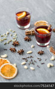 christmas and seasonal drinks concept - hot mulled wine, dry orange slices, raisins with cashew nuts and aromatic spices on grey background. hot mulled wine, orange slices, raisins and spices