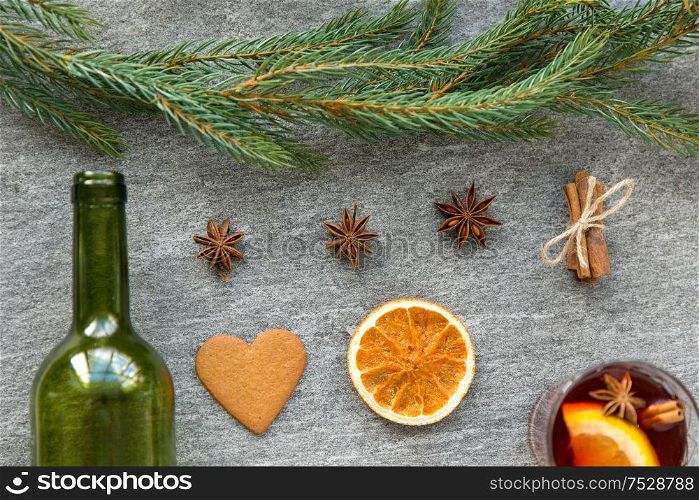 christmas and seasonal drinks concept - hot mulled wine, empty green glass bottle, dry orange slices, gingerbread and aromatic spices on grey background. mulled wine, orange slices, gingerbread and spices